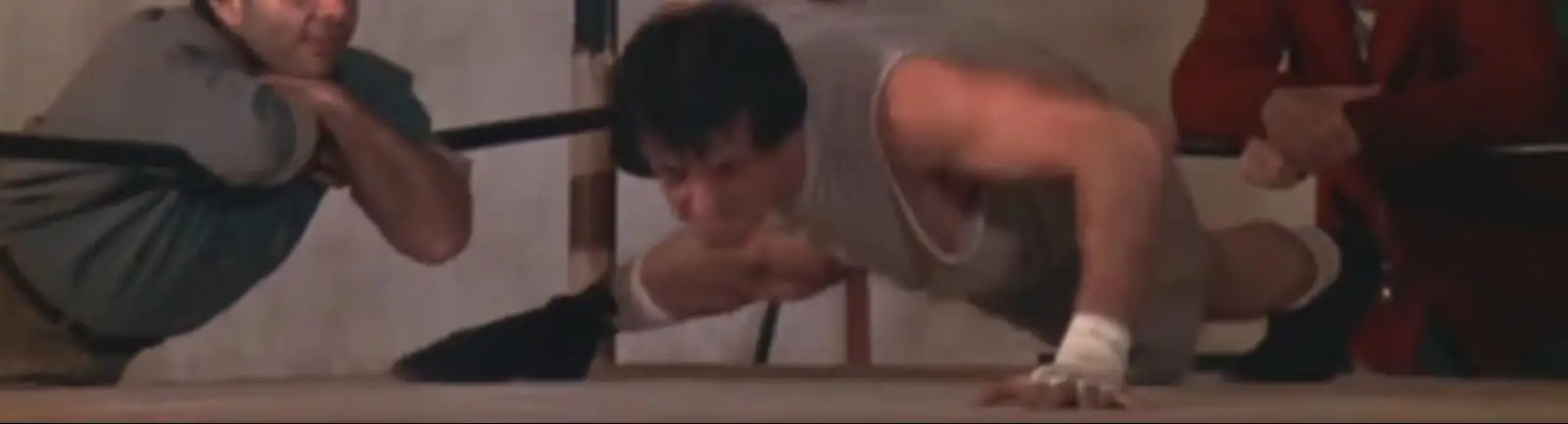 Rocky doing pushups with coach and team mate looking outside the boxing ring