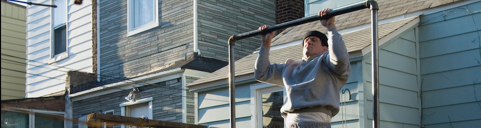 Rocky BalBoa doing chin ups outside a house