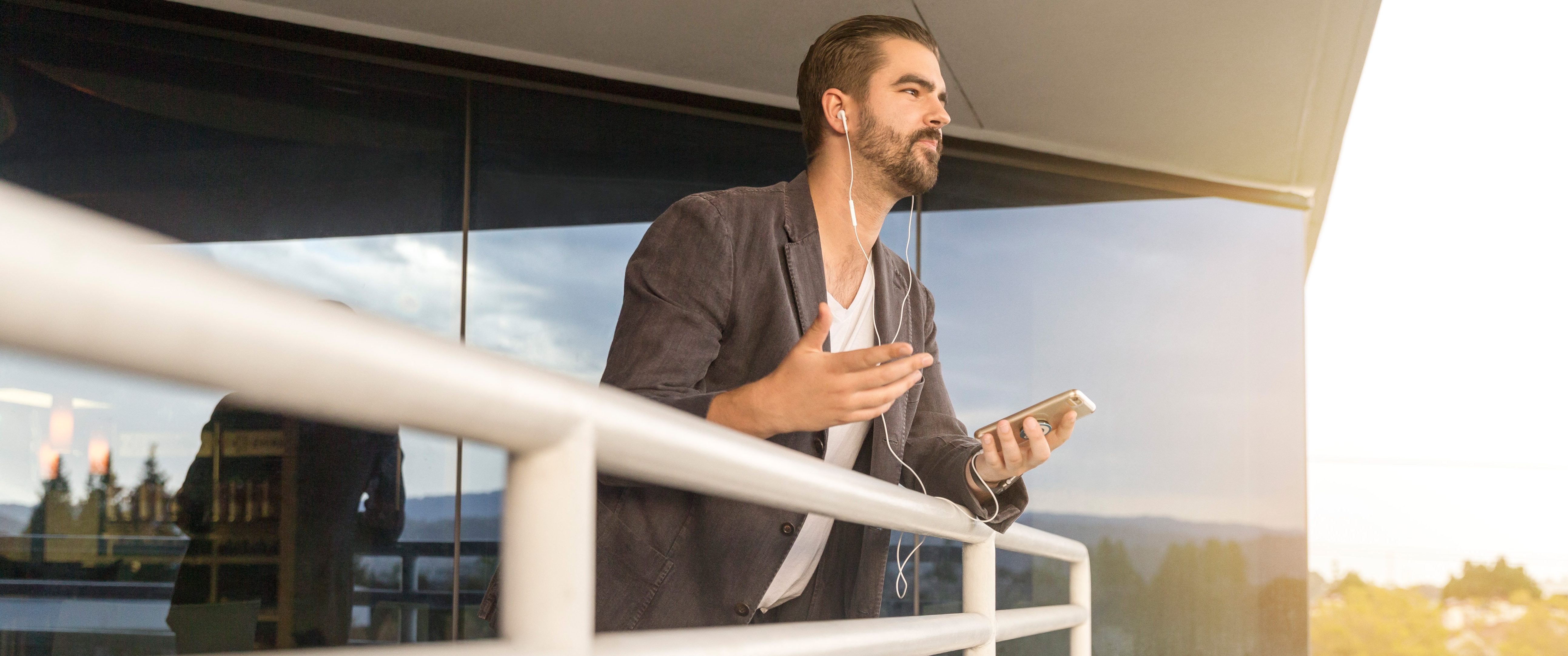Man with sport jacket talking on iPhone with headset over a railing